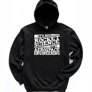 May include: Black hooded sweatshirt with a front pocket and white text that reads "IT'S NOT ROCKET SCIENCE IT'S AEROSPACE ENGINEERING". The sweatshirt has a drawstring hood and long sleeves.