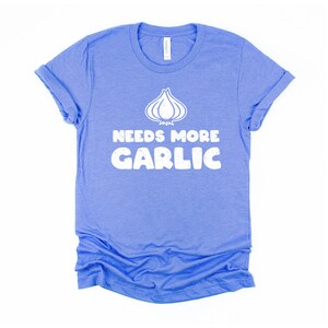 May include: A blue t-shirt with a white graphic of a garlic clove and the text "Needs More Garlic".