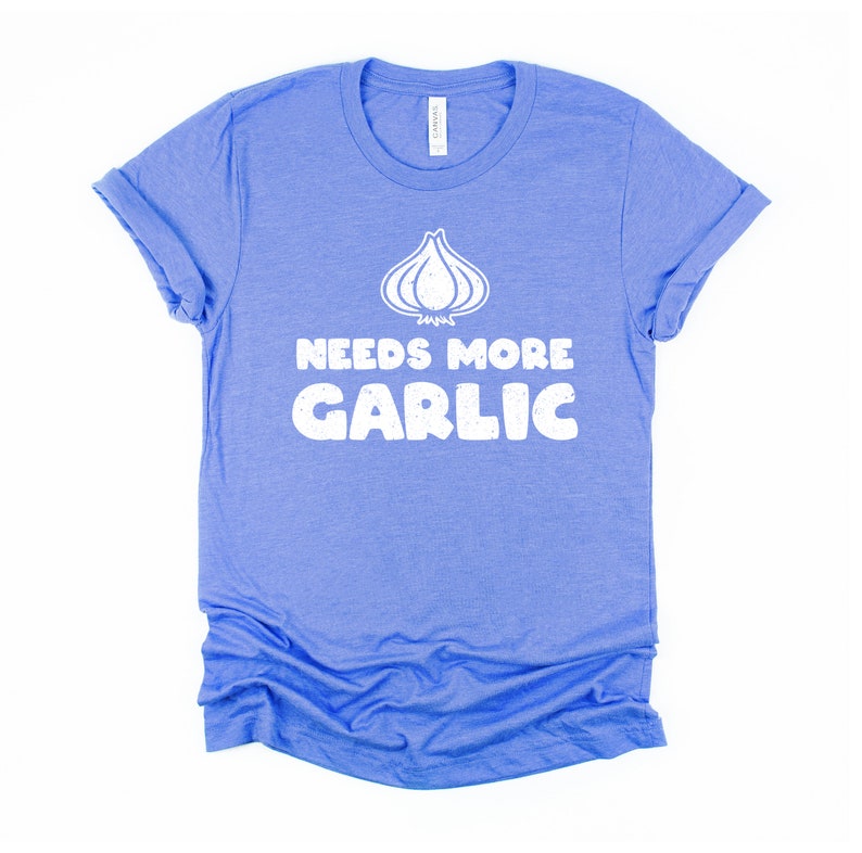 May include: A blue t-shirt with a white graphic of a garlic clove and the text "Needs More Garlic".