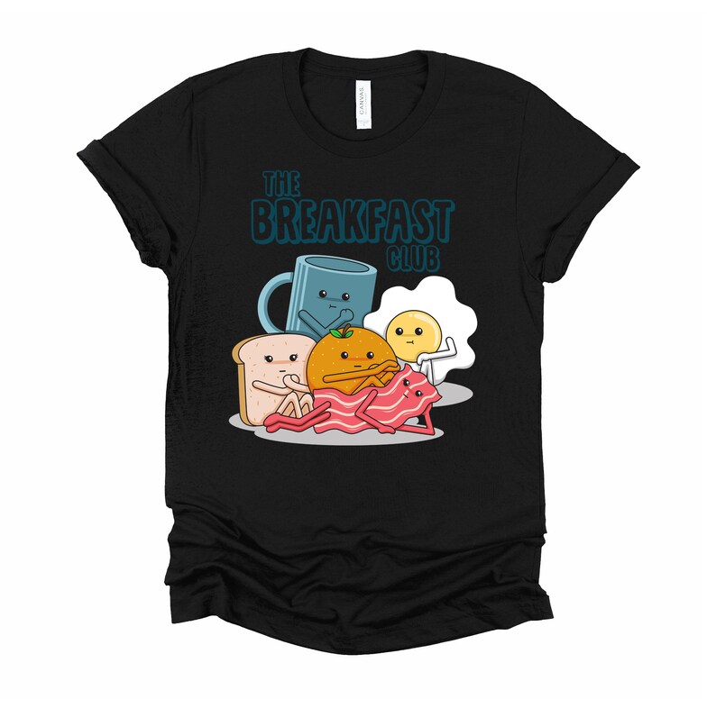 May include: Black t-shirt featuring a graphic of breakfast foods, including a cup of coffee, an orange, a slice of toast, bacon, and an egg. The text "The Breakfast Club" is printed above the graphic.