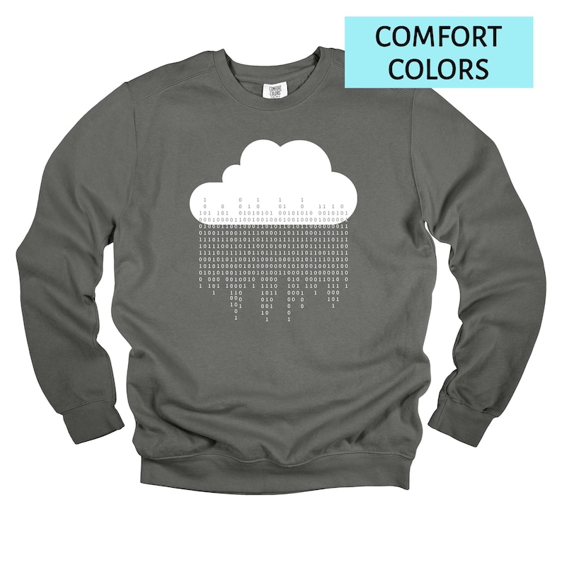 Op de afbeelding: Een donkergrijs sweatshirt met een witte wolkengrafiek waaruit binaire code regent. De tekst "COMFORT COLORS" staat in een lichtblauwe rechthoek. De sweatshirt heeft lange mouwen en een ronde hals.