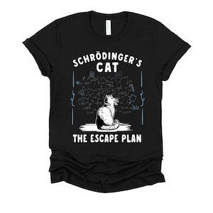 May include: A black short-sleeve t-shirt featuring a white graphic of a cat sitting in front of complex mathematical equations. The text reads "SCHRÖDINGER'S CAT" above the cat and "THE ESCAPE PLAN" below the cat in white capital letters.