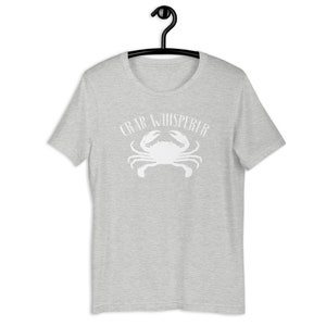May include: A heather grey t-shirt with a white crab silhouette and the text "Crab Whisperer" printed on the front.