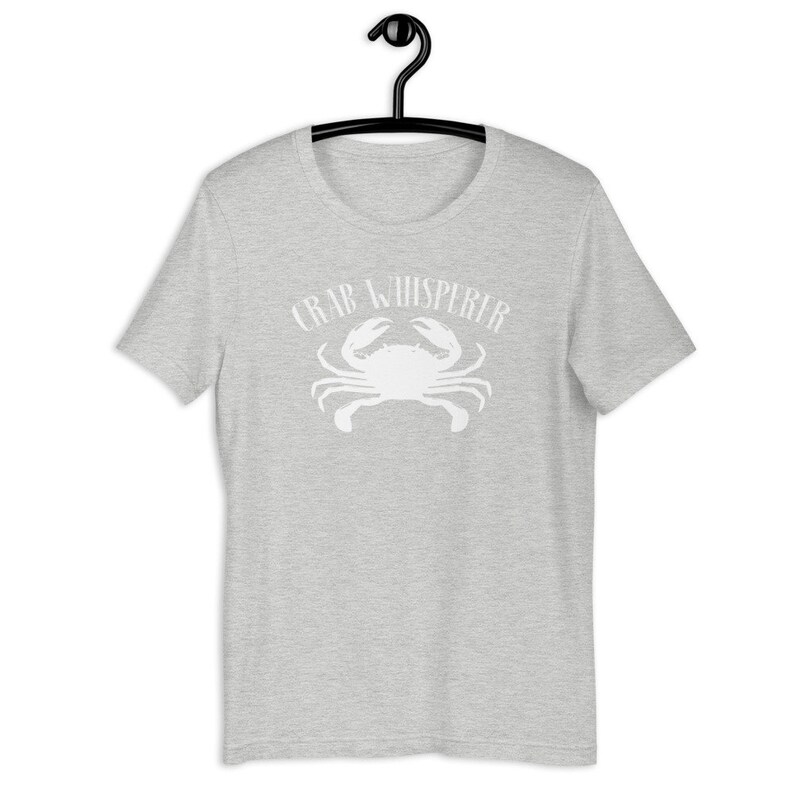 May include: A heather grey t-shirt with a white crab silhouette and the text "Crab Whisperer" printed on the front.