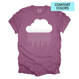 Pode incluir: Camiseta malva com um desenho de nuvem branca e c&oacute;digo bin&aacute;rio representando a chuva. O texto "COMFORT COLORS" est&aacute; em um ret&acirc;ngulo azul claro. A camisa tem um ajuste confort&aacute;vel.