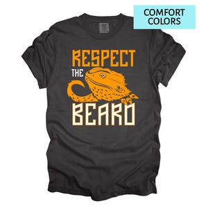May include: Dark gray t-shirt with the text "Respect the Beard" in orange and white. The design features an orange bearded dragon illustration. The words "Comfort Colors" are in a light blue box in the upper right corner.