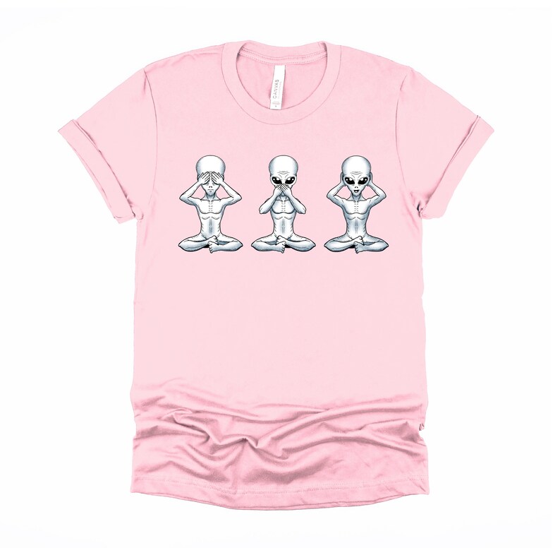 May include: Pink t-shirt featuring a graphic of three grey aliens in a row, each with one hand covering their eyes, one hand covering their ears, and one hand covering their mouth. The aliens are sitting in a yoga pose.