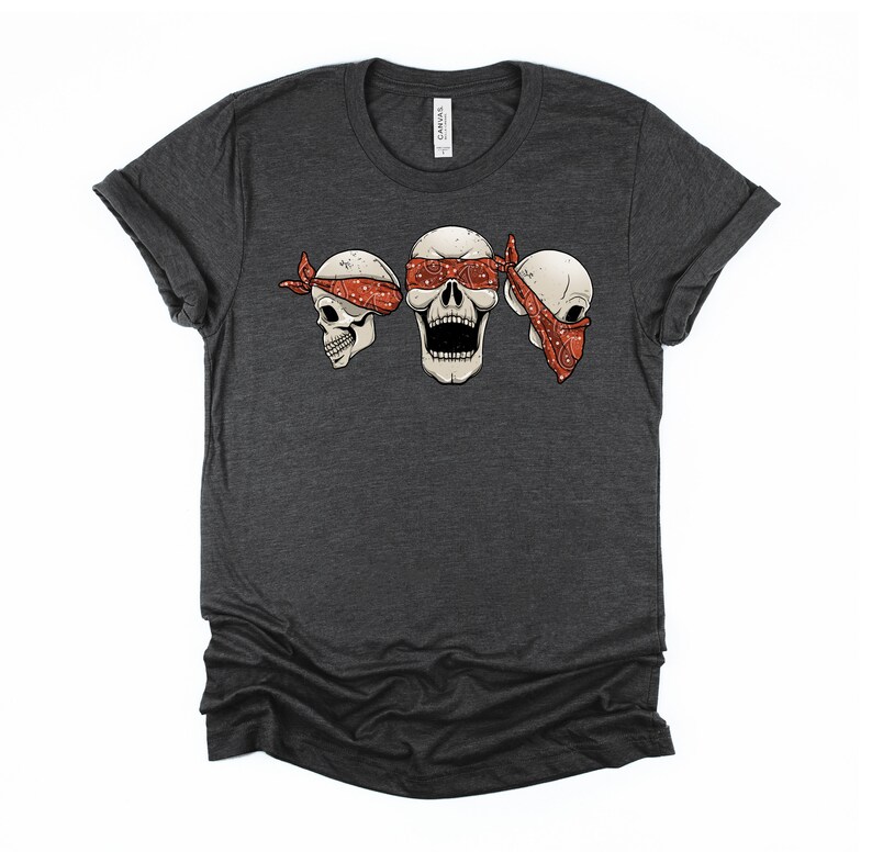 May include: A dark heather grey t-shirt with a graphic of three skulls wearing red bandanas. The skulls are blindfolded with the bandanas.