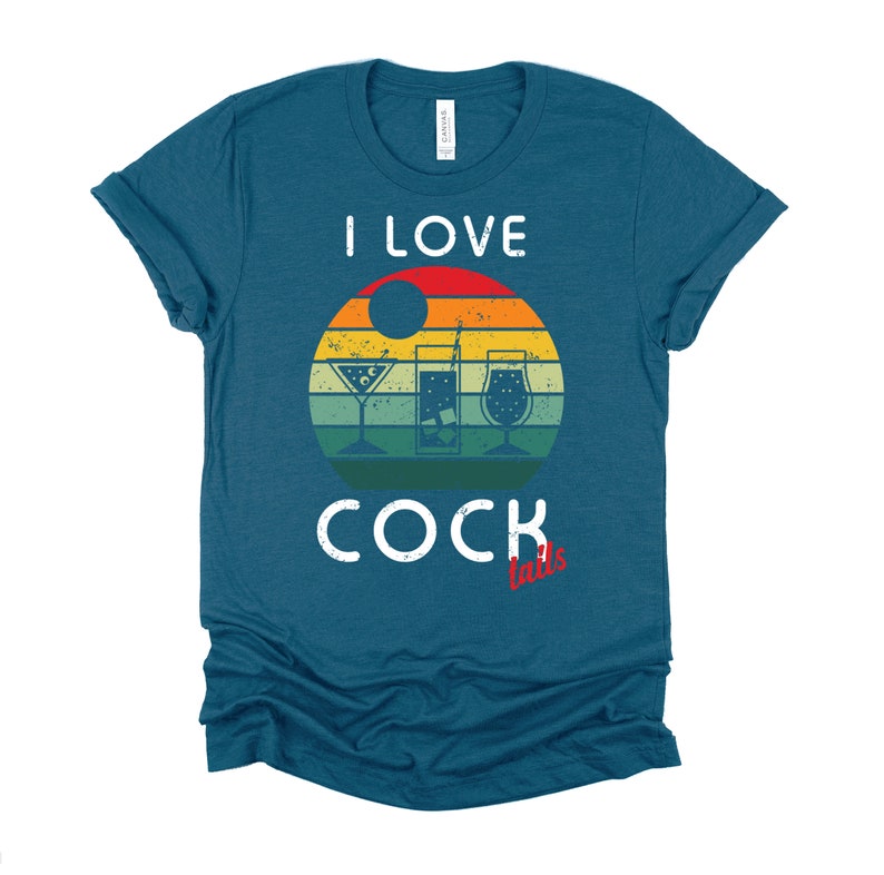 Op de afbeelding: Een tealblauw t-shirt met een vintage-stijl grafische afbeelding van een zonsondergang met drie cocktailglazen. De tekst "Ik hou van cocktails" is op het shirt gedrukt.