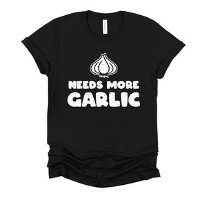 May include: Black t-shirt with a white graphic of a garlic bulb and the text "Needs More Garlic".