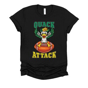 May include: Black t-shirt featuring a cartoon duck with green and yellow wings, a yellow and white head, and a football. The text "QUACK ATTACK" is above and below the duck and football illustration.