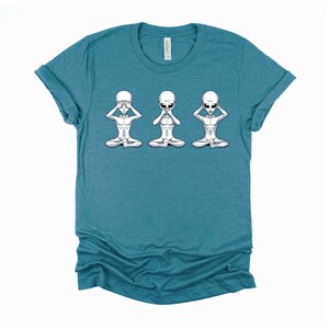 May include: A teal blue t-shirt featuring a graphic of three grey aliens in a yoga pose. The aliens are covering their eyes, mouth, and ears.