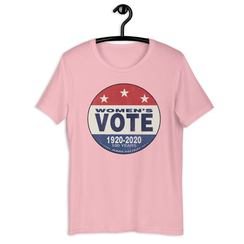 May include: Pink t-shirt with a vintage-style button featuring the text "Women's Vote" and the years "1920-2020" with the text "100 Years 19th Amendment" underneath.