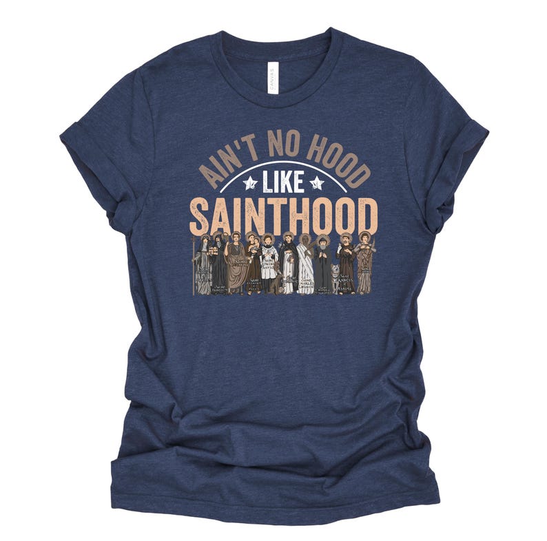 Pu&ograve; includere: T-shirt blu navy con la scritta "Ain't No Hood Like Sainthood" in marrone e bianco. La grafica include illustrazioni di varie figure. La maglietta &egrave; realizzata in un materiale morbido.