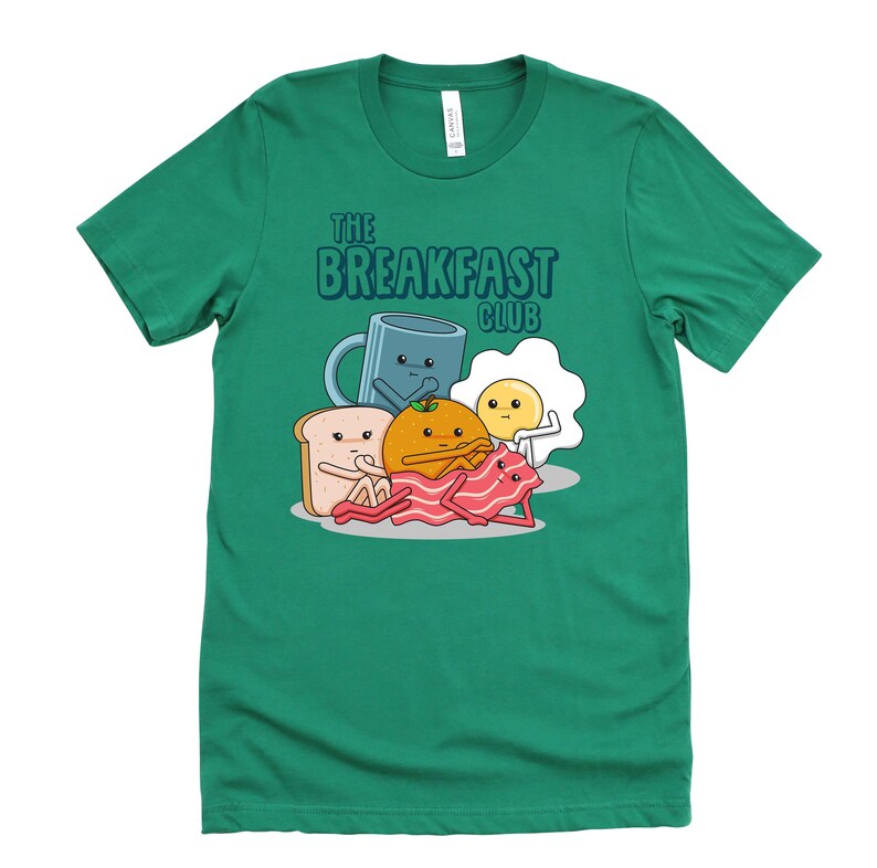 May include: A green t-shirt featuring a cartoon illustration of breakfast foods. The text "The Breakfast Club" is printed on the shirt.