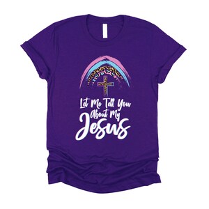 May include: Purple t-shirt with a rainbow and cross graphic. The text "Let Me Tell You About My Jesus" is printed on the shirt.