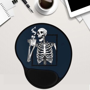 May include: A blue and black mouse mat with a skeleton holding a cup of coffee. The skeleton is in a white outline and the coffee cup is black. The mouse mat has a black wrist rest.