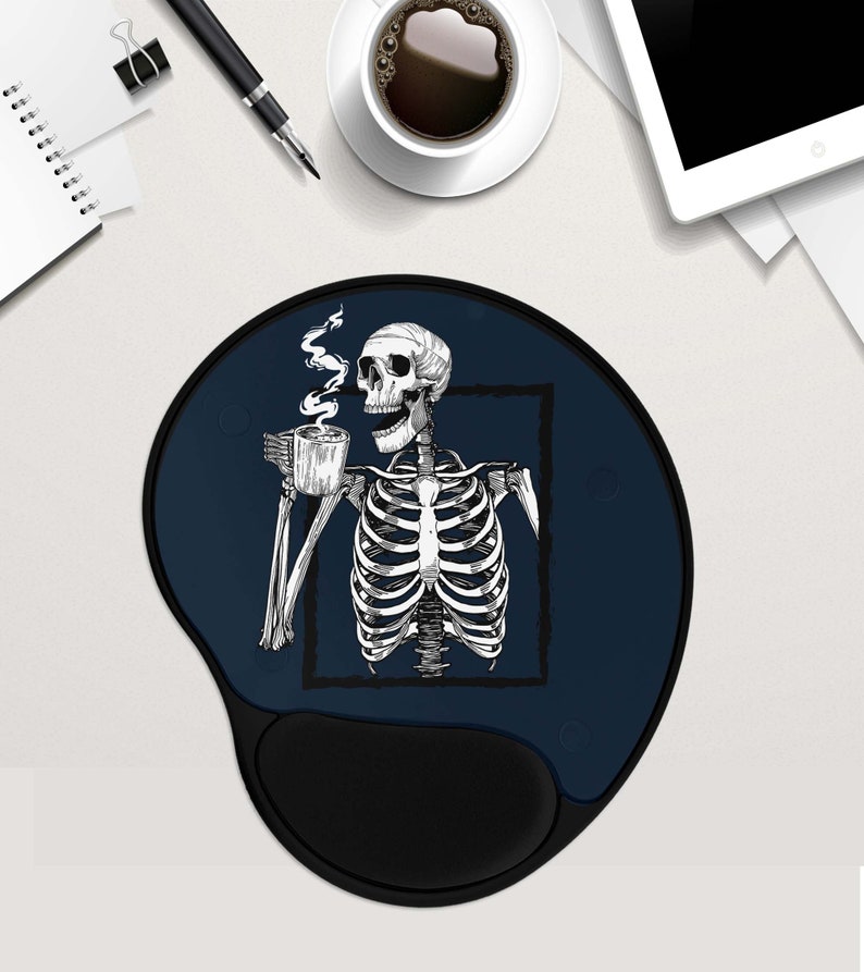 May include: A blue and black mouse mat with a skeleton holding a cup of coffee. The skeleton is in a white outline and the coffee cup is black. The mouse mat has a black wrist rest.