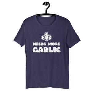 May include: A navy blue t-shirt with a white graphic of a garlic clove and the text "Needs More Garlic".