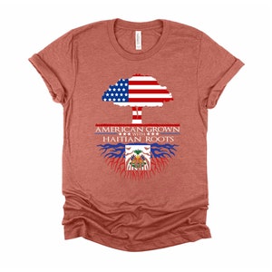 May include: A heather red t-shirt with a graphic of an American flag tree with Haitian flag roots. The text "American Grown with Haitian Roots" is printed on the shirt.