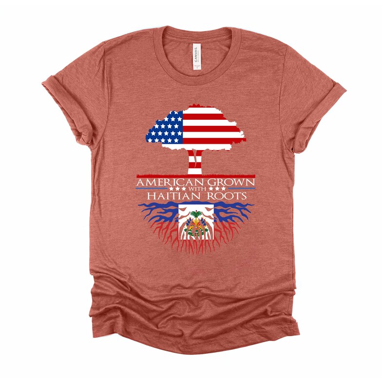May include: A heather red t-shirt with a graphic of an American flag tree with Haitian flag roots. The text "American Grown with Haitian Roots" is printed on the shirt.