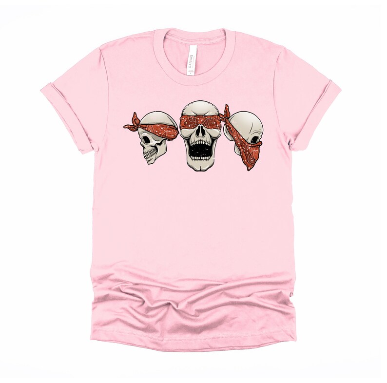 May include: Pink t-shirt with three white skulls wearing red bandanas. The middle skull has its eyes covered by the bandana.
