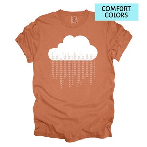 Pode incluir: Camiseta cor de ferrugem com um gr&aacute;fico de nuvem branca e chuva de c&oacute;digo bin&aacute;rio. O texto "COMFORT COLORS" est&aacute; em um ret&acirc;ngulo azul claro. A camiseta tem gola redonda e mangas curtas.