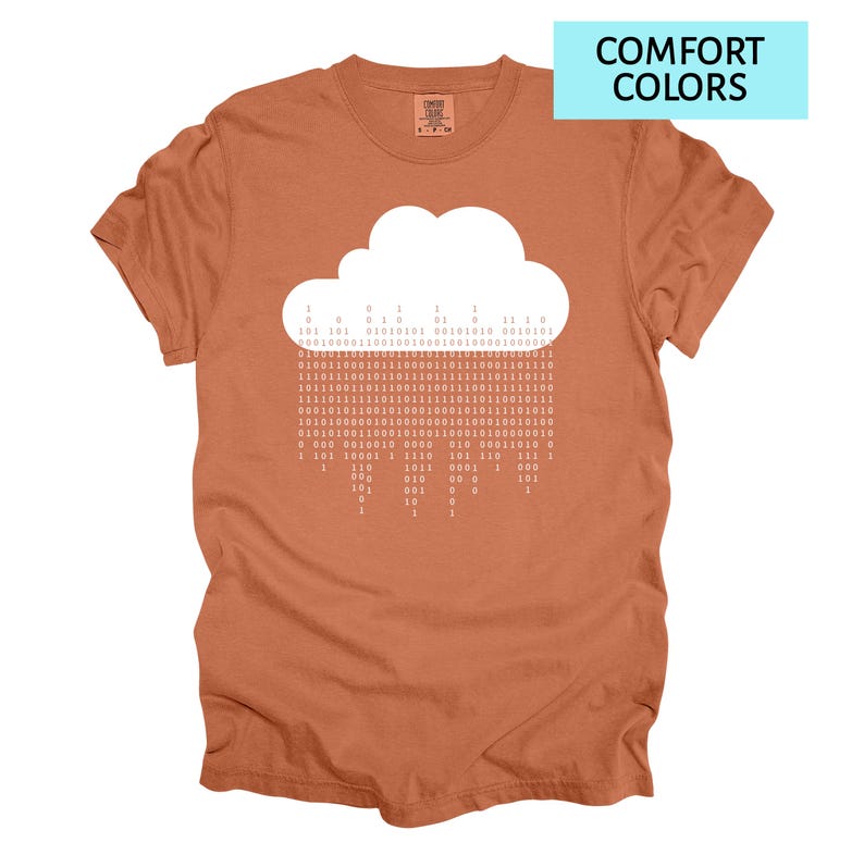 Pode incluir: Camiseta cor de ferrugem com um gr&aacute;fico de nuvem branca e chuva de c&oacute;digo bin&aacute;rio. O texto "COMFORT COLORS" est&aacute; em um ret&acirc;ngulo azul claro. A camiseta tem gola redonda e mangas curtas.