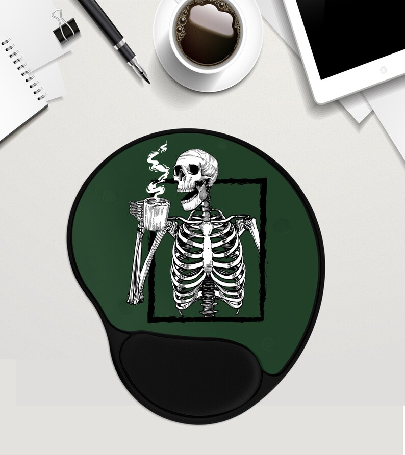 May include: Green round mouse mat with a black skeleton holding a cup of coffee. The skeleton is inside a white square frame. The mouse mat has a black wrist rest.