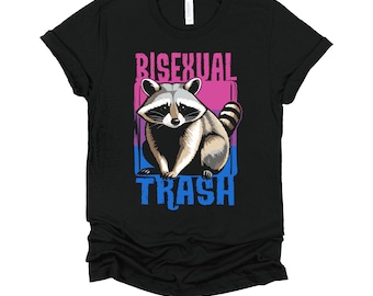 May include: Black t-shirt featuring a raccoon illustration with the text "BISEXUAL TRASH" in pink and blue. The raccoon is depicted in shades of gray and brown, with a striped tail.