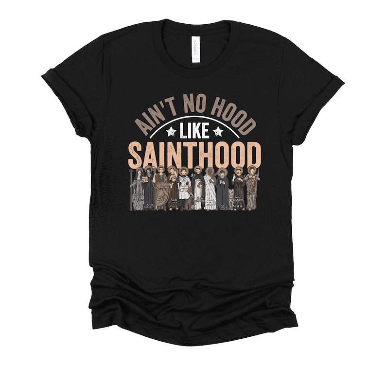 Pu&ograve; includere: T-shirt nero con la scritta "Ain't No Hood Like Sainthood" in un design circolare. Sotto il testo, un'illustrazione di figure in abiti religiosi. La maglietta &egrave; realizzata in materiale morbido.