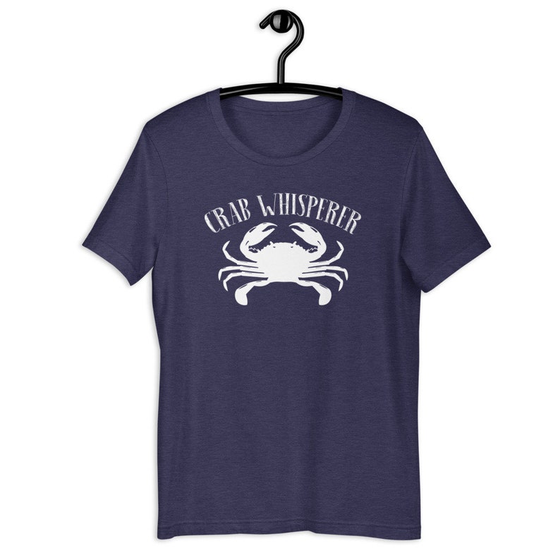 May include: A navy blue t-shirt with a white crab graphic and the text "CRAB WHISPERER" printed on the front.