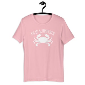 May include: Pink t-shirt with a white crab and the text "Crab Whisperer" printed on the front.