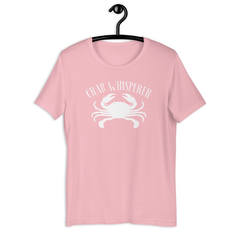 May include: Pink t-shirt with a white crab and the text "Crab Whisperer" printed on the front.