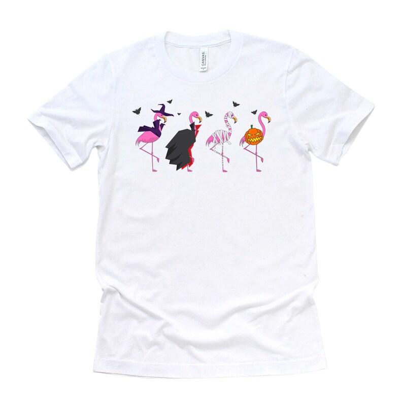 May include: White t-shirt with a graphic of four pink flamingos dressed in Halloween costumes. The flamingos are dressed as a witch, a vampire, a mummy, and a pumpkin.