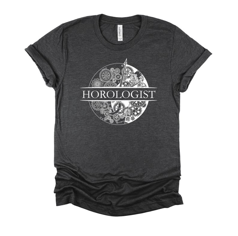 May include: A dark gray t-shirt with a white graphic of a clock face with gears and the word "HOROLOGIST" printed across the center.