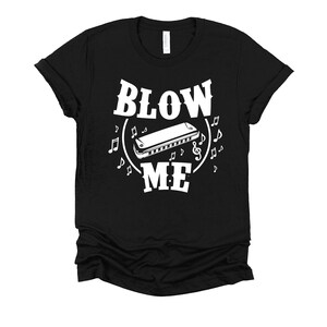 May include: Black t-shirt with white text that reads "Blow Me" and a graphic of a harmonica with musical notes.