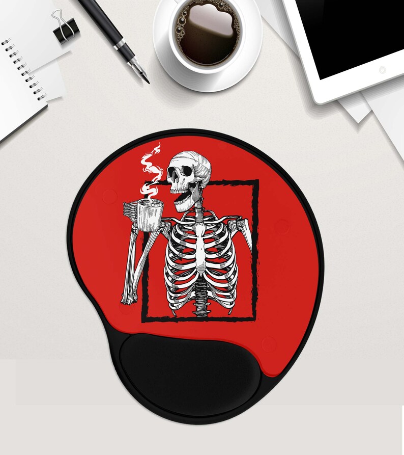 May include: Red mouse mat with a black skeleton holding a cup of coffee. The skeleton is inside a black square frame. The mouse mat has a black, rounded wrist rest.