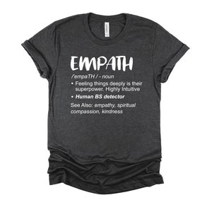 May include: Dark gray t-shirt with white text that reads "EMPATH /'empaTH/ - noun • Feeling things deeply is their superpower. Highly Intuitive • Human BS detector See Also: empathy, spiritual compassion, kindness"