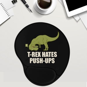 May include: A black and green mouse pad with a cartoon T-Rex dinosaur doing a push-up. The text "T-Rex hates push-ups" is printed on the mouse pad.