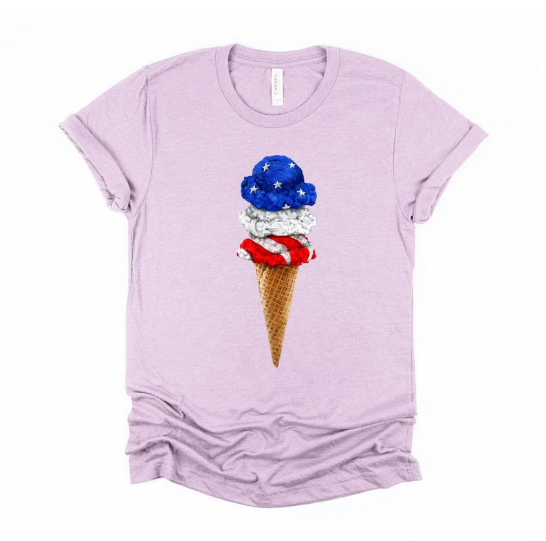 May include: A light purple t-shirt with a graphic of a three-scoop ice cream cone. The ice cream is decorated with red, white, and blue to resemble the American flag.