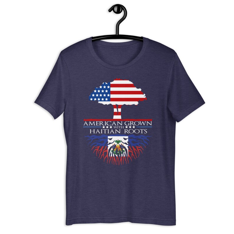 May include: A navy blue t-shirt with a tree design. The tree's trunk is brown, the leaves are the American flag, and the roots are the Haitian flag. The text "AMERICAN GROWN WITH HAITIAN ROOTS" is printed on the shirt.