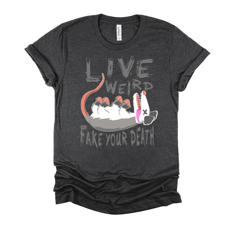 Op de afbeelding: Een donker grijs t-shirt met een afbeelding van een opossum die dood speelt en de tekst "Live Weird Fake Your Death".