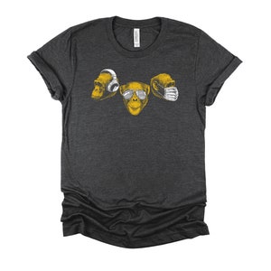 May include: A dark gray t-shirt with a graphic of three monkeys. The monkey on the left is wearing headphones, the monkey in the middle is wearing sunglasses, and the monkey on the right is wearing a face mask.