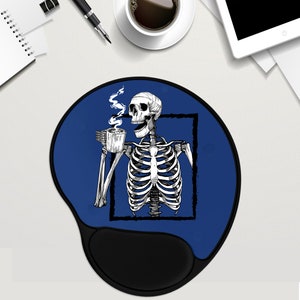 May include: A blue round mouse mat with a black skeleton holding a cup of coffee. The skeleton is inside a white square frame. The mouse mat has a black, ergonomic wrist rest.