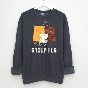 May include: A dark blue sweatshirt with a graphic of a graham cracker, marshmallow, and chocolate bar hugging each other. The text "GROUP HUG" is printed below the graphic.