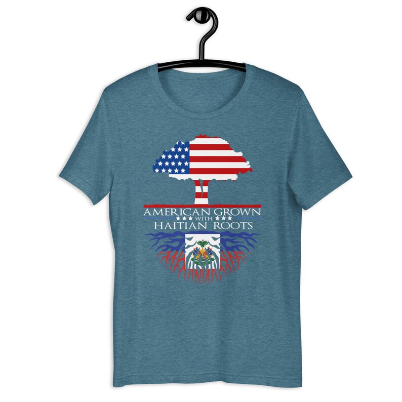 May include: A teal blue t-shirt with a graphic of a tree with the American flag as the leaves and Haitian flag as the roots. The text "American Grown with Haitian Roots" is printed on the shirt.