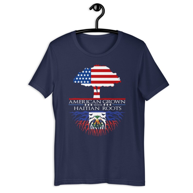 May include: Navy blue t-shirt with a tree design. The tree's trunk is brown and the leaves are the American flag. The roots are the Haitian flag. The text reads "American Grown with Haitian Roots".