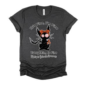 May include: Dark gray t-shirt with a distressed graphic of a black cat with an orange bow and ribbon. Text reads "It's Fine, I'm Fine" and "Everything Is Fine Multiple Sclerosis Awareness". The shirt has rolled sleeves.