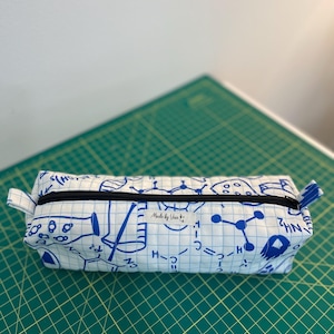 May include: A white pencil case with a blue and black science themed print. The case has a zipper closure and a label that reads "Made by Yar".
